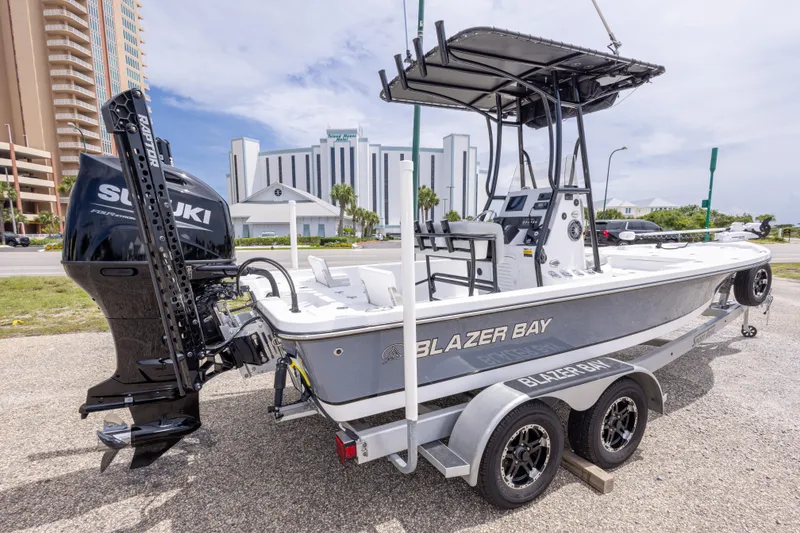 Slide: The Image of 2023 Blazer Bay 2200 boat on trailer with Suzuki engine, parked near buildings. - 12