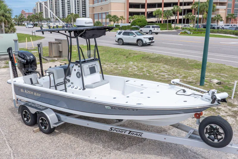 Slide: The Image of 2023 Blazer Bay 2200 boat on trailer, parked near a road with buildings in background. - 2