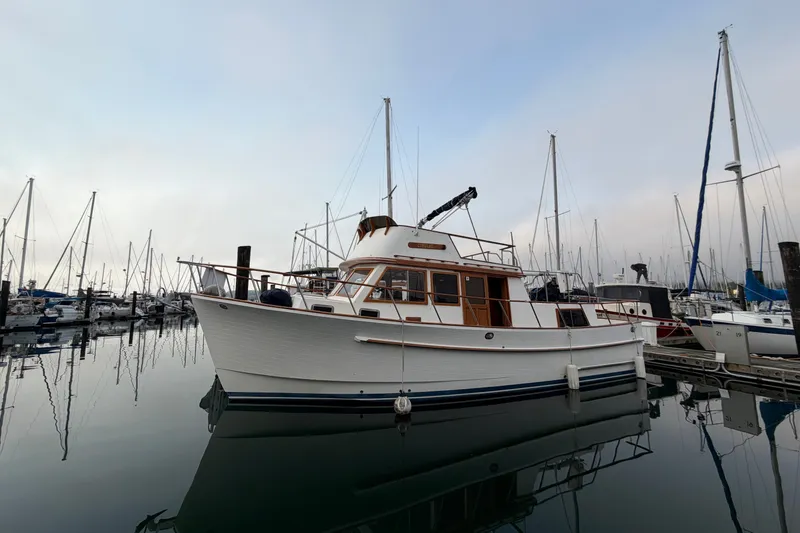 Slide: The Image of 1988 Monk 36 yacht docked in a marina, surrounded by sailboats under a cloudy sky. - 1