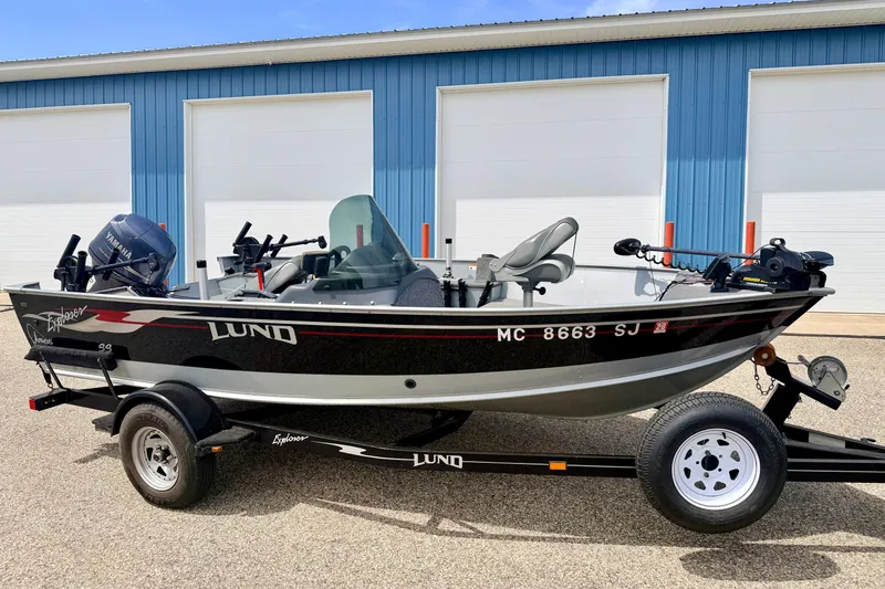 The Image of 2003 Lund 1675 Adventure SS boat on trailer, parked outside blue building. - 0