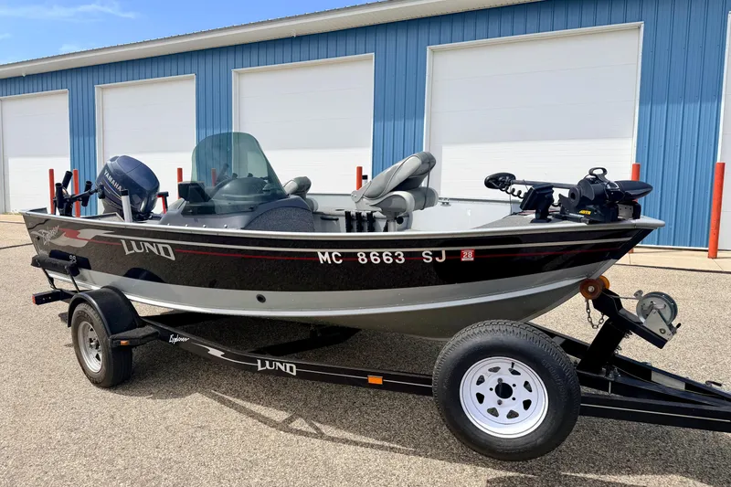 Slide: The Image of 2003 Lund 1675 Adventure SS boat on trailer, parked near blue building. - 2