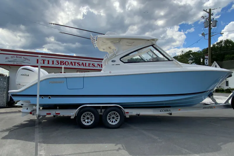 The Image of 2026 Pursuit DC 286 Dual Console boat on trailer at dealership, cloudy sky background. - 1