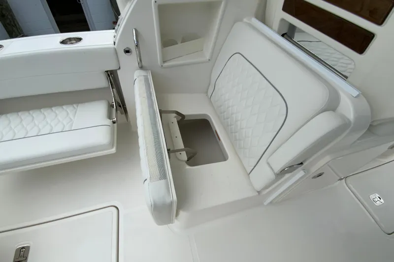 Slide: The Image of 2026 Pursuit DC 286 Dual Console boat interior with white cushioned seating and storage compartment. - 22