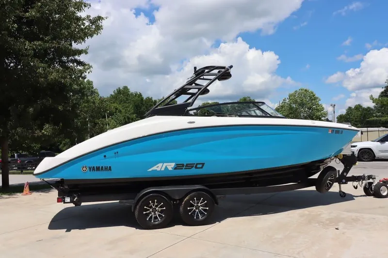The Image of 2023 Yamaha Boats AR250 in blue, parked on a trailer under a sunny sky. - 0