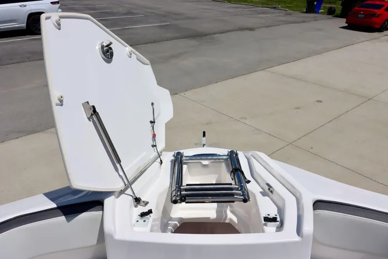 Slide: The Image of 2023 Yamaha Boats AR250 bow storage compartment with ladder, open in a parking area. - 20
