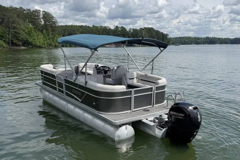 Slide: The Image of 2023 Godfrey Sweetwater 2286 C pontoon boat on a serene lake with a Mercury outboard motor. - 3