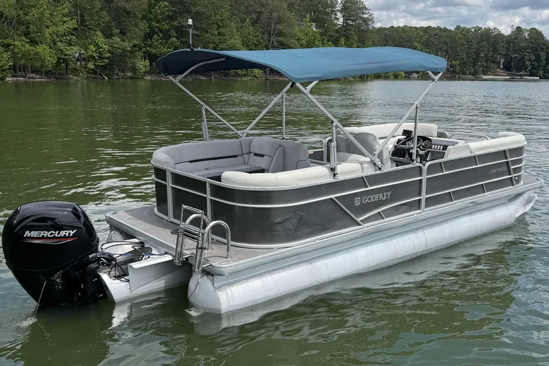 Slide: The Image of 2023 Godfrey Sweetwater 2286 C pontoon boat with Mercury engine on a serene lake. - 5