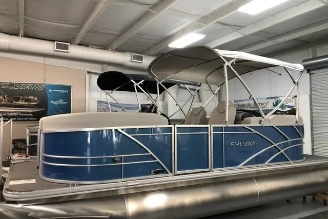 The Image of 2024 Sylvan Mirage 820 LZ pontoon boat in showroom, featuring blue exterior and canopy. - 0