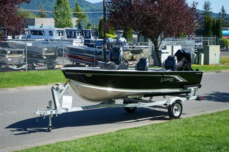 Slide: The Image of 2026 Lund 1400 Fury SS boat on trailer, parked outdoors near dealership. - 8