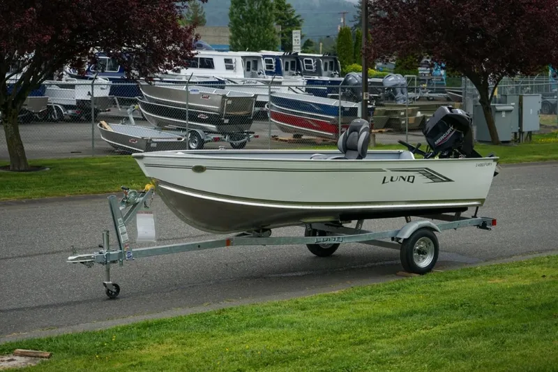 Slide: The Image of 2026 Lund 1400 Fury Tiller boat on trailer, parked near marina with other boats. - 15