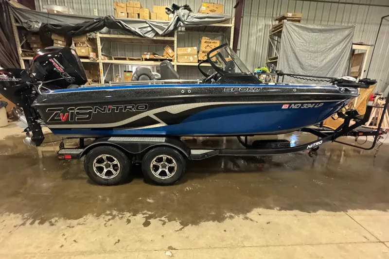 The Image of 2021 Nitro ZV19 Sport boat in a garage, blue and black design, on a trailer. - 0