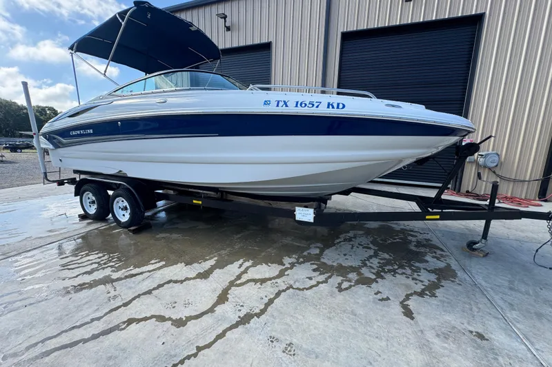 The Image of 2005 Crownline 240 EX boat on trailer, parked outside a warehouse. - 1
