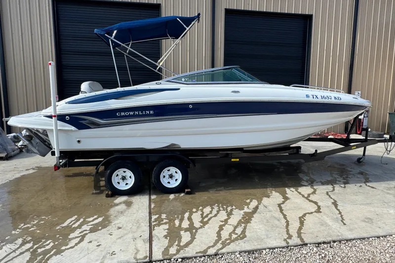 Slide: The Image of 2005 Crownline 240 EX boat on trailer with blue canopy, parked outside a building. - 3