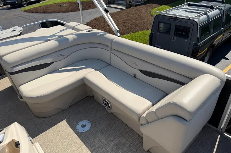 Slide: The Image of 2018 Bennington 21 SF boat with beige seating and speaker, parked near a vehicle. - 3