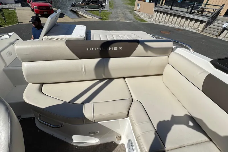 Slide: The Image of 2018 Bayliner 195 Deck Boat interior with beige seating and logo. - 3