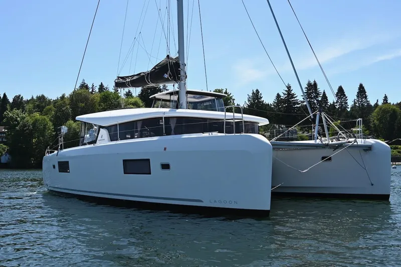 Slide: The Image of 2022 Lagoon 42 catamaran sailing on a serene lake with lush greenery. - 2