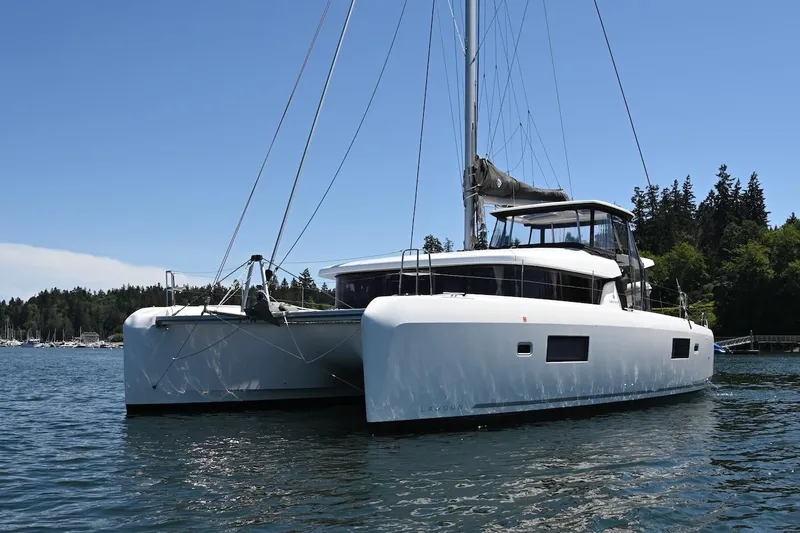 Slide: The Image of 2022 Lagoon 42 catamaran sailing on calm waters near a forested shoreline. - 5