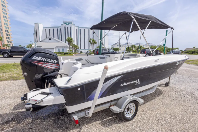 Slide: The Image of 2015 Bayliner Element XL boat with Mercury engine on trailer, parked near buildings. - 11