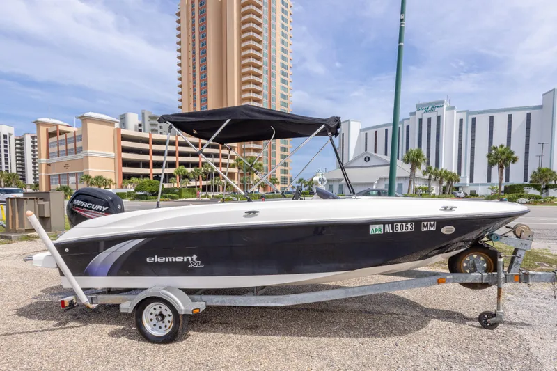 Slide: The Image of 2015 Bayliner Element XL boat on trailer, parked near tall buildings. - 5