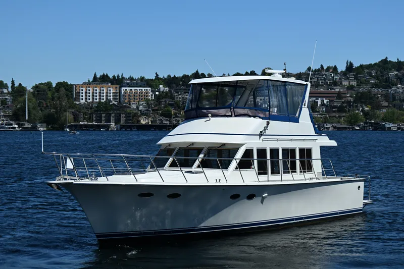 Slide: The Image of 1999 McKinna 47 Sedan yacht cruising on a scenic lake with city backdrop. - 4