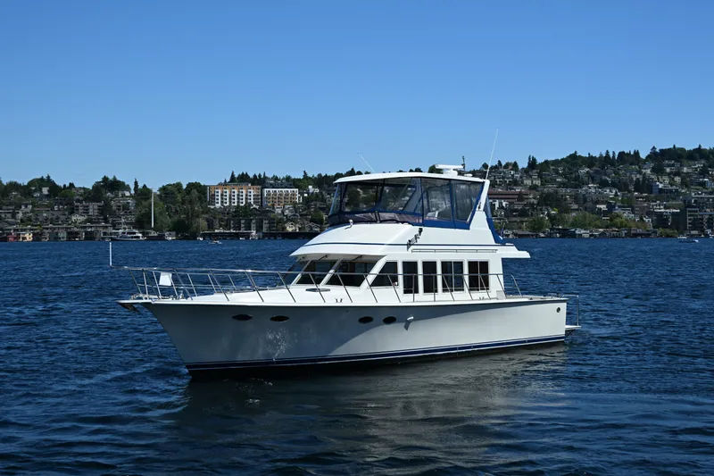 Slide: The Image of 1999 McKinna 47 Sedan yacht cruising on a scenic lake with cityscape background. - 5