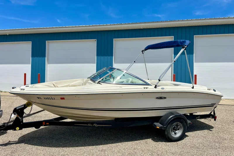The Image of 2001 Sea Ray 182 Bow Rider boat on trailer, parked outside blue building. - 0