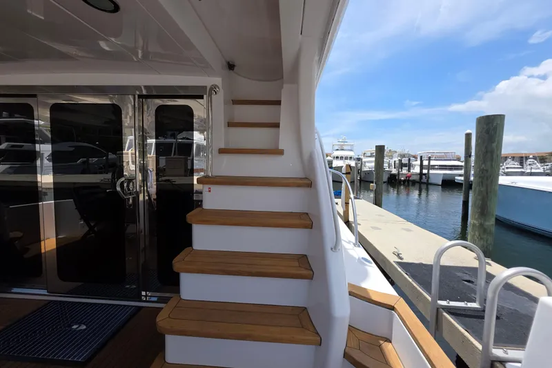 Slide: The Image of 2008 Hatteras 64 Motor Yacht docked, featuring elegant wooden steps and glass doors. - 13