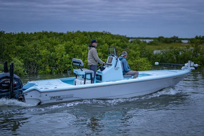 The Image of 2025 Pathfinder 2300 HPS boat navigating through calm waters near lush greenery. - 0