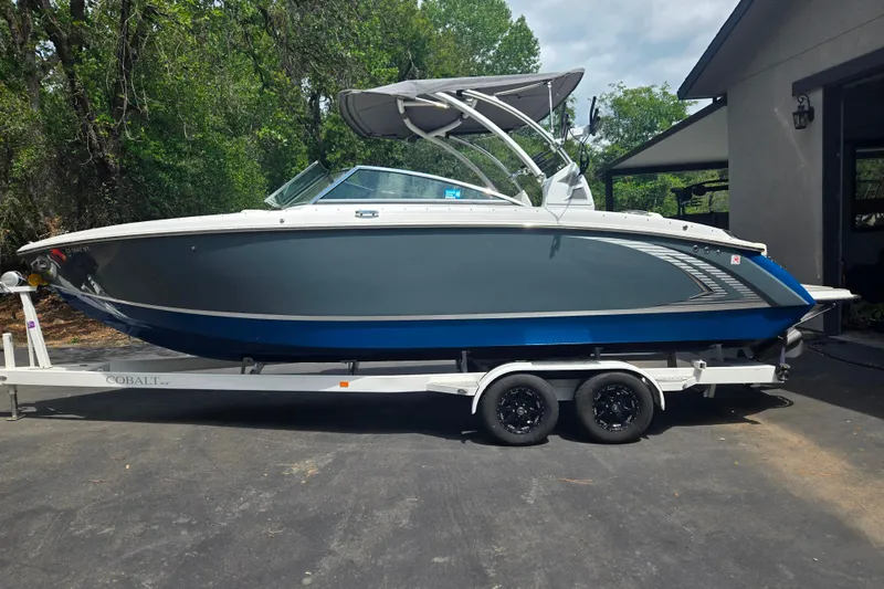 Slide: The Image of 2020 Cobalt R7 Surf boat on trailer, parked outdoors near trees and a building. - 17