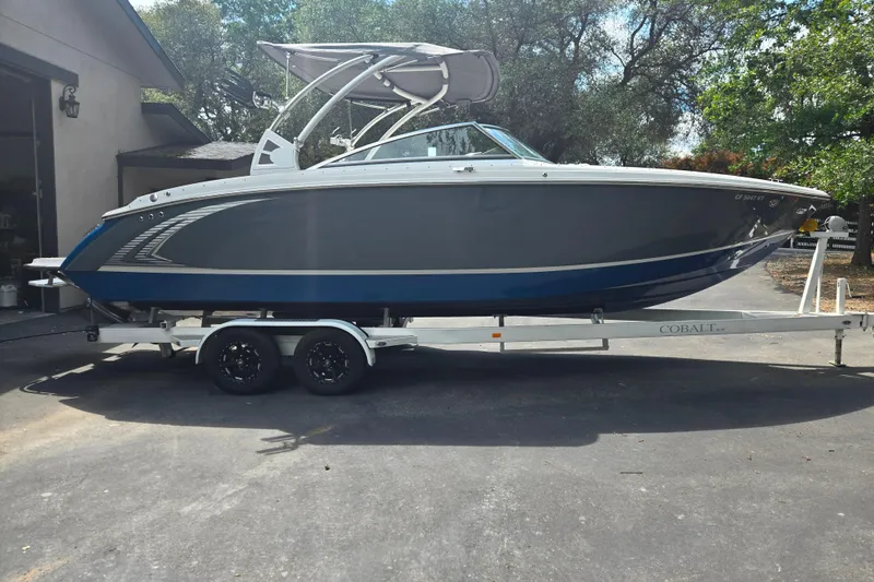 Slide: The Image of 2020 Cobalt R7 Surf boat on trailer, parked outdoors, surrounded by trees. - 19