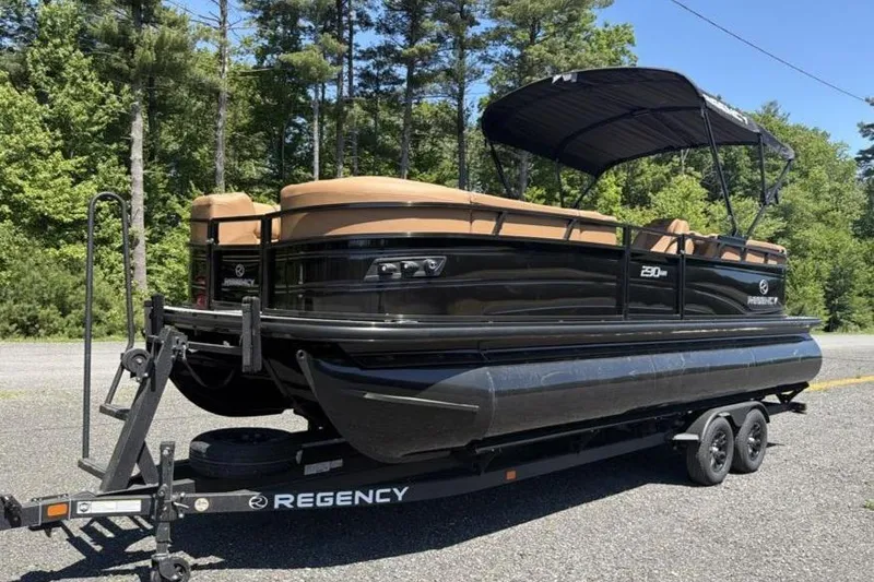 The Image of 2026 Regency 230 DL pontoon boat on trailer, parked outdoors with trees in background. - 0