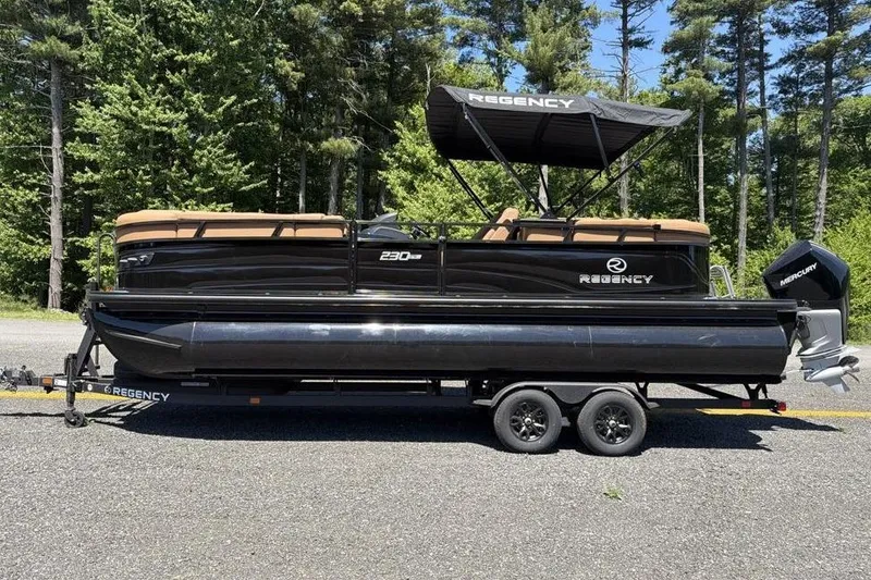 Slide: The Image of 2026 Regency 230 DL pontoon boat on trailer, parked outdoors with forest background. - 1