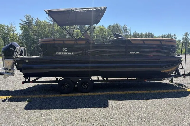 Slide: The Image of 2026 Regency 230 DL pontoon boat on trailer, parked outdoors with trees in background. - 4