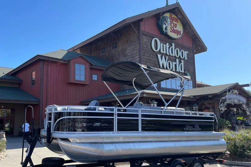 The Image of 2026 Sun Tracker SportFish 20 DLX pontoon boat displayed outside Bass Pro Shops Outdoor World. - 0