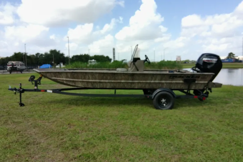 Slide: The Image of 2026 Tracker Grizzly 1860 CC boat on trailer, parked on grassy area near water. - 10
