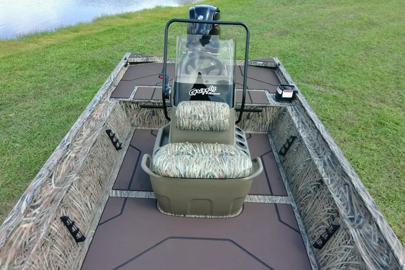 Slide: The Image of 2026 Tracker Grizzly 1860 CC boat with camo seats, on grassy terrain near water. - 17