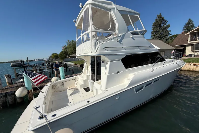 Slide: The Image of 2001 Silverton 42 Convertible yacht docked by waterfront homes, featuring spacious deck and American flag. - 2