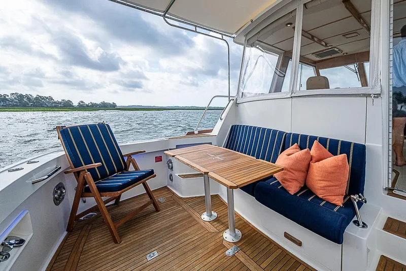 Slide: The Image of 2004 Grand Banks 49 Eastbay HX yacht deck with seating, table, and scenic water view. - 7