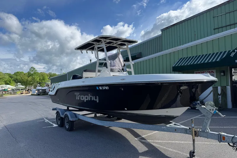 Slide: The Image of 2021 Trophy T22CX boat on trailer outside a green building under a cloudy sky. - 2