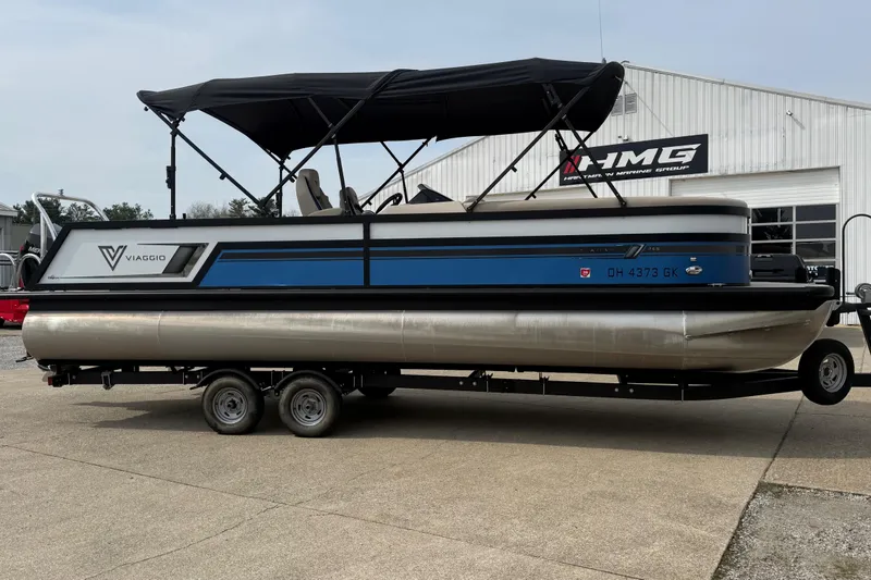 Slide: The Image of 2022 Viaggio Diamante S 26 pontoon boat on trailer, parked outside a marine shop. - 4