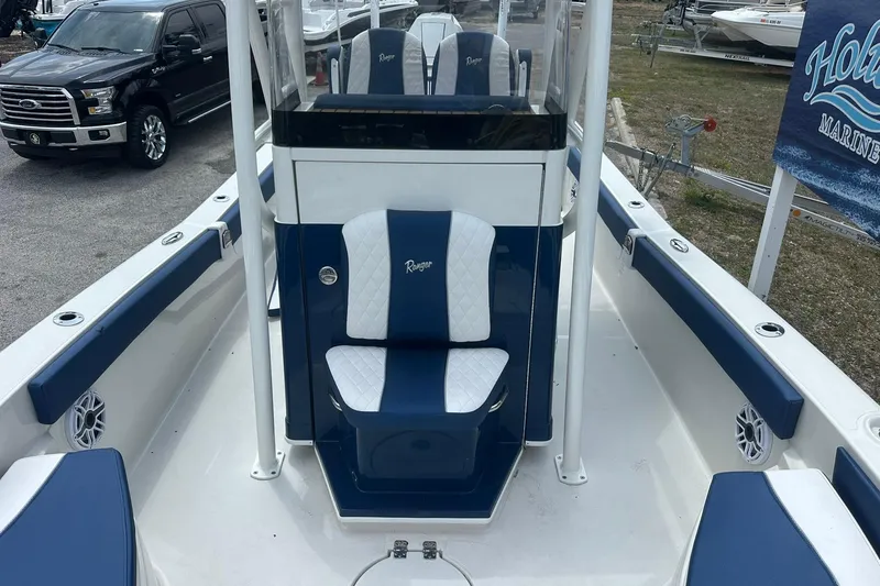 Slide: The Image of 2026 Ranger 2660 Bay boat interior with blue and white seating, parked near vehicles. - 16