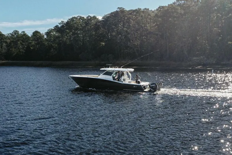 Slide: The Image of 2020 Scout 380 LXF boat cruising on a serene lake with forest backdrop. - 5