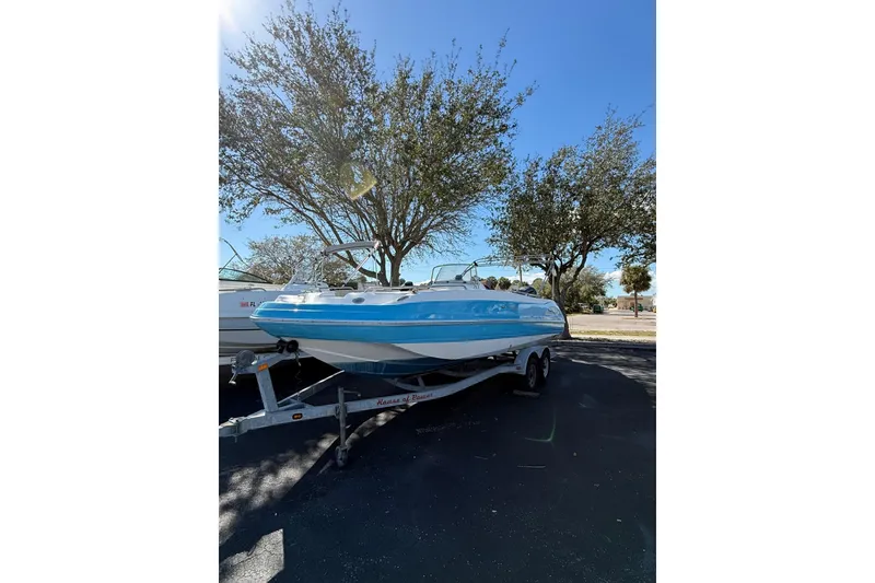 The Image of 2019 Hurricane SunDeck Sport CC 231 OB boat on trailer, parked under clear blue sky. - 1