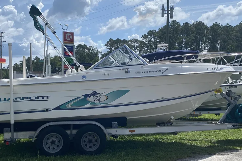 The Image of 2001 Aquasport 215 Osprey Sport boat on trailer, parked outdoors under a cloudy sky. - 1