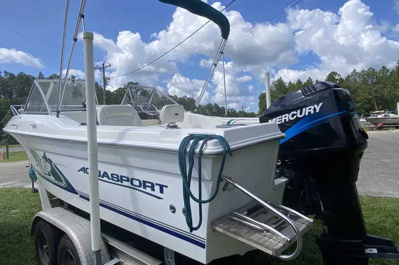 Slide: The Image of 2001 Aquasport 215 Osprey Sport boat with Mercury engine on trailer, under blue sky. - 2