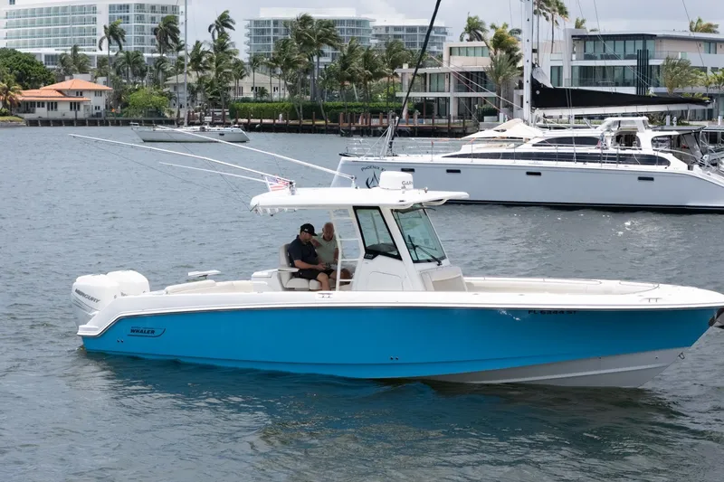 The Image of 2020 Boston Whaler 330 Outrage boat cruising on a scenic waterfront with luxury yachts. - 0
