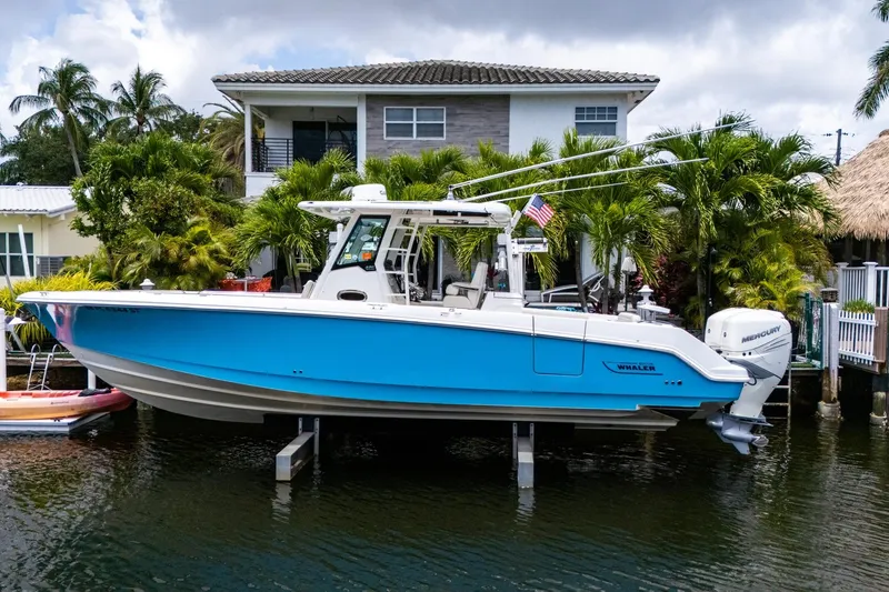 Slide: The Image of 2020 Boston Whaler 330 Outrage boat docked by a waterfront home with palm trees. - 2