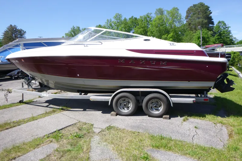 The Image of 1998 Maxum 2300 SC boat on trailer, parked outdoors with lush greenery. - 1