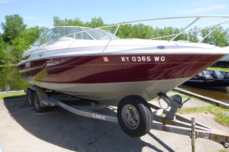 Slide: The Image of 1998 Maxum 2300 SC boat on trailer, parked near a lake with lush greenery. - 5
