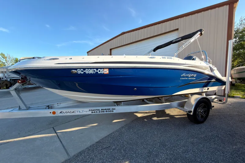 Slide: The Image of 2022 Hurricane SunDeck Sport 205 OB boat on trailer, blue and white design, parked outdoors. - 1